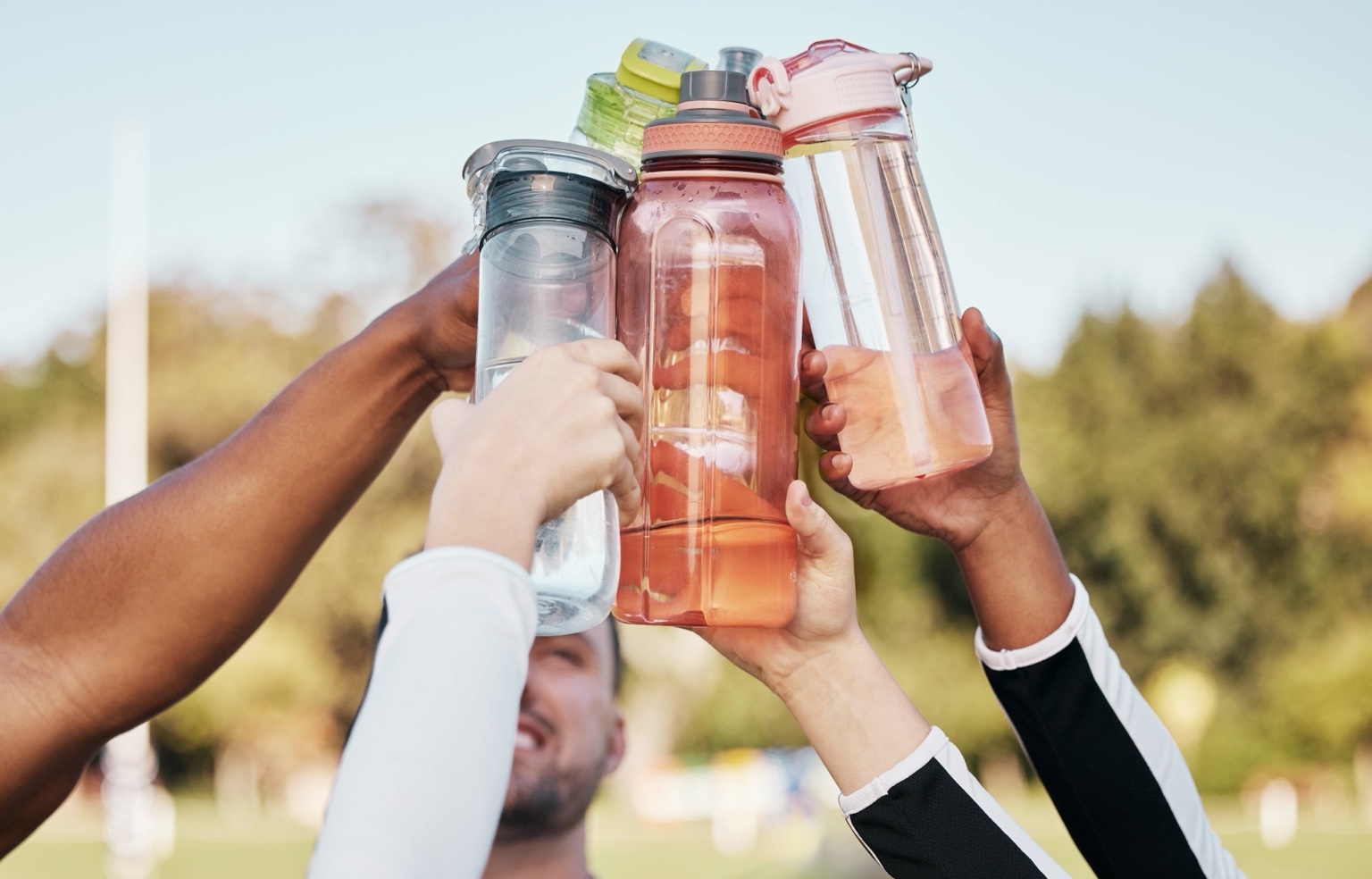 Friends raising their reusable water bottles together outdoors